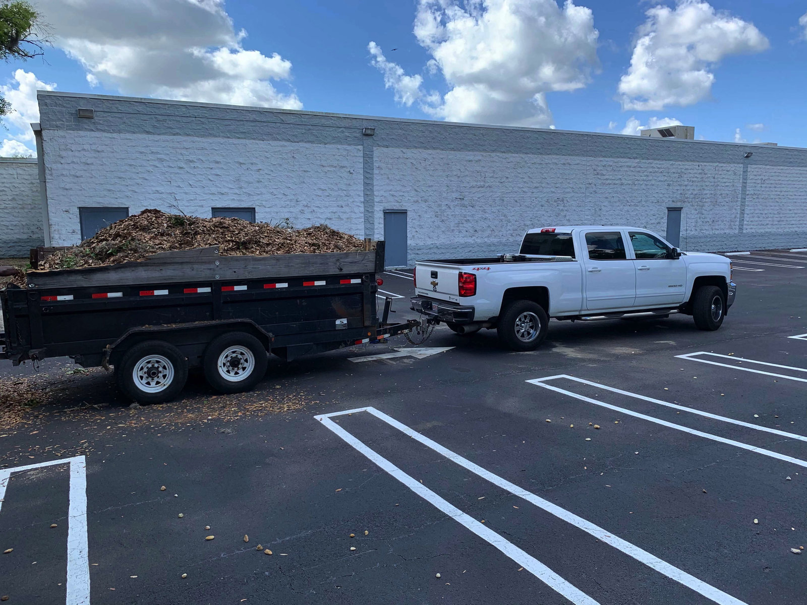 Trailer loaded with yard material beside a pickup truck in a parking lot