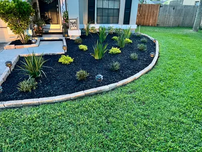 Curved landscape bed with black mulch, white edging and fresh plants by a front porch