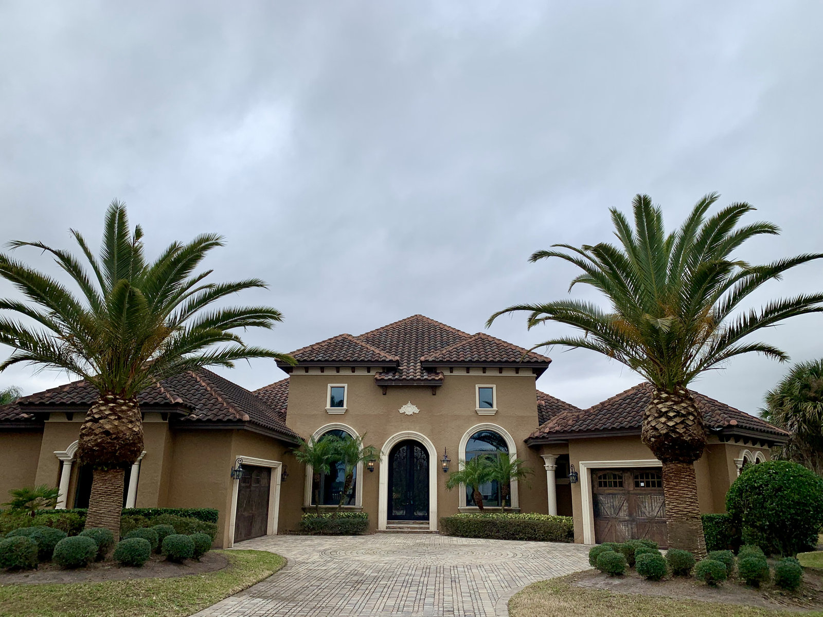 Mediterranean-style Florida home with two tall palms, clipped shrubs and a neat front lawn